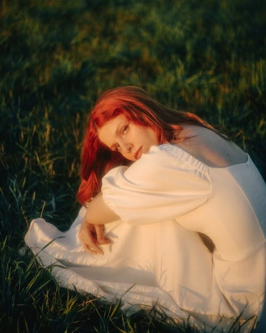 Model in a Long White Dress Sitting on a Meadow