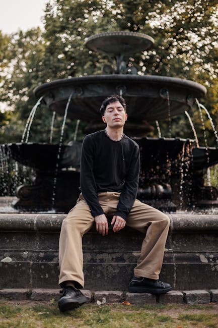 A young man sitting on a bench in front of a fountain