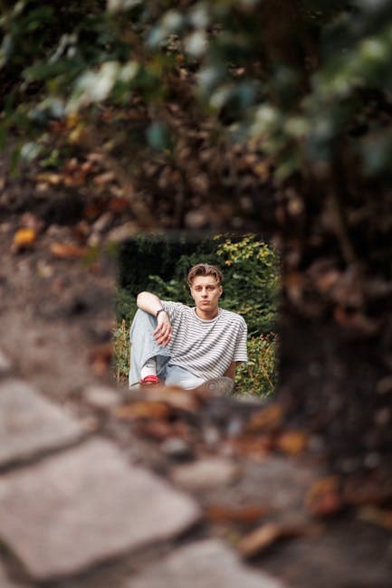 A young man sitting on the ground in front of bushes