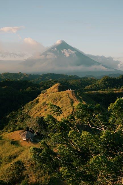 A mountain with a green grassy hill and a volcano in the background