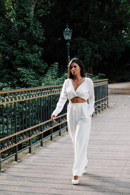 A woman in white pants and a white top walking on a bridge