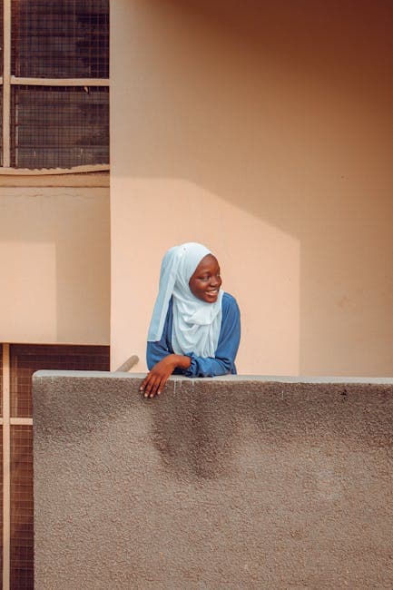 A woman in a blue hijab leaning against a wall