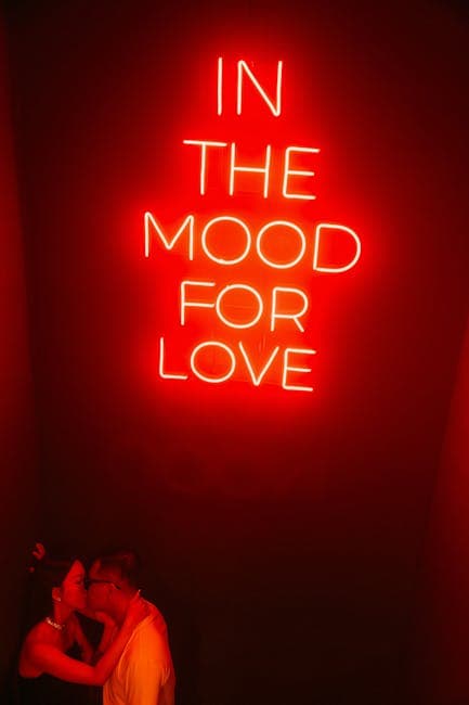 A couple kissing in front of a neon sign that says in the mood for love