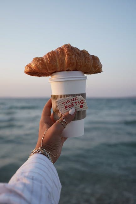 A person holding a coffee cup with a croissant on top