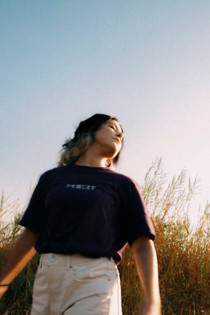 A woman standing in tall grass wearing a purple shirt