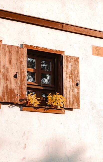 Close-up of a Window with Wooden Shutters and Plants on the Windowsill 