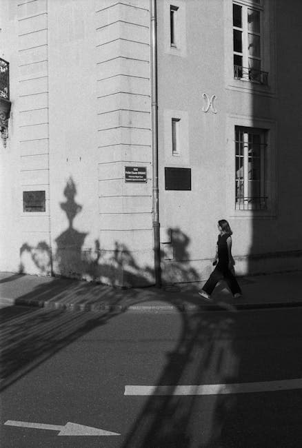 Black and White Photo of a Woman Walking on the Sidewalk 