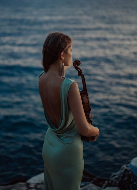 Woman in Dress Standing with Violin on Sea Shore