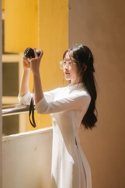 A Young Woman Wearing a White Ao Dai Holding a Camera 