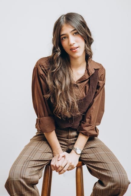 Long-Haired Brunette Wearing a Brown Top Sitting on a Stool