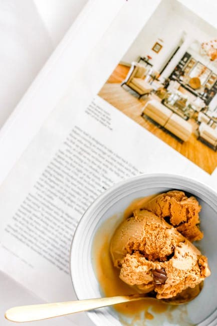 A scoop of ice cream sits on a table next to a magazine