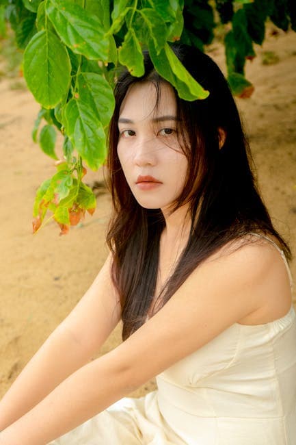 Brunette Woman in White Dress Sitting Under Green Leaves