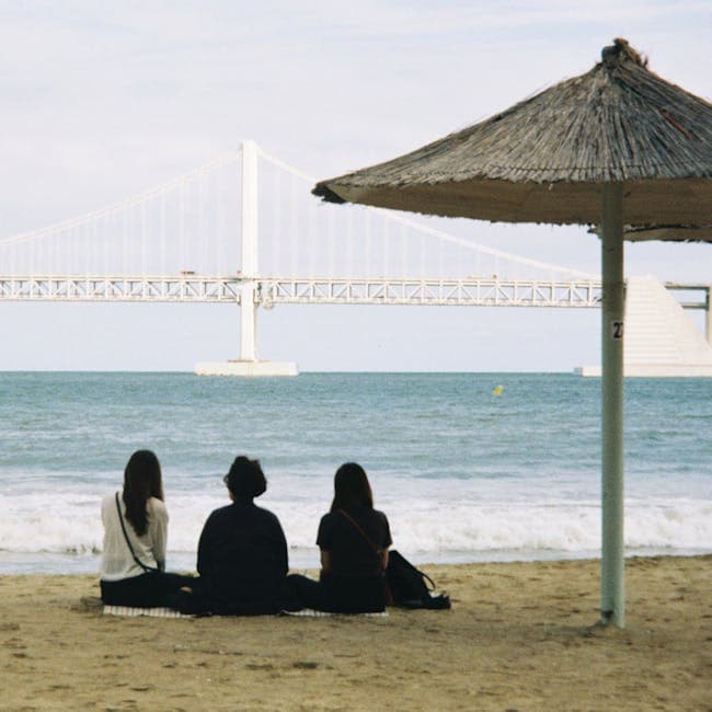 Three people sitting on the beach under an umbrella