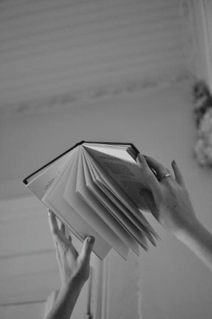 Black and White Photo of Open Book Held by Hands