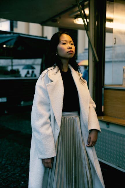 Stylish woman in white coat on urban street at dusk